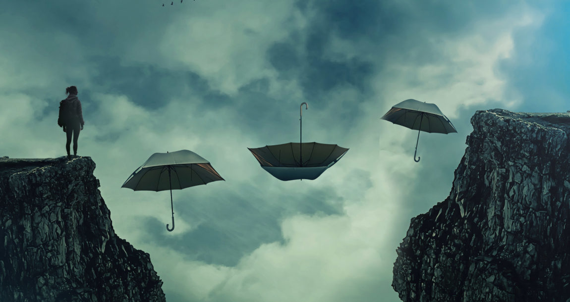 Image showing a woman looking over the edge of a cliff, separated from another cliff by 3 floating umbrellas.