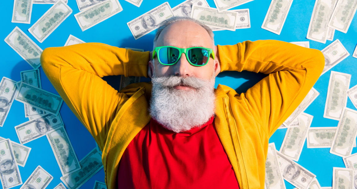 Senior man in sunglasses relaxing, laying on a bed of money.