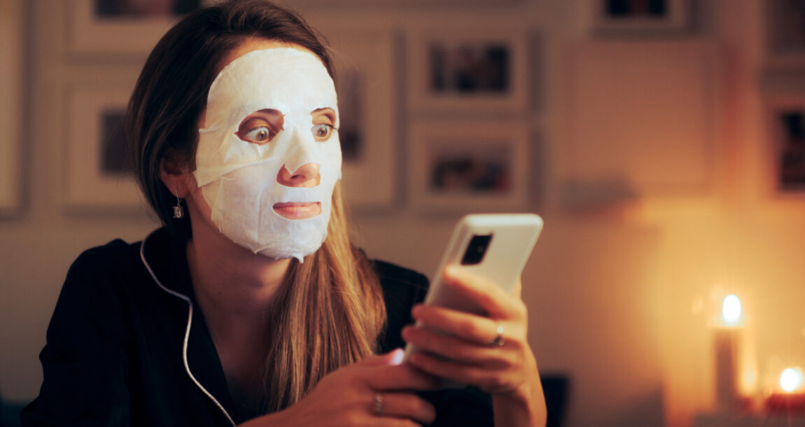 Woman with a beauty mask on looking at her phone