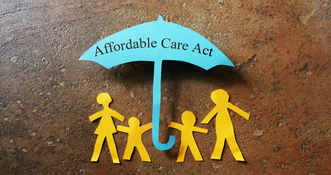 Image showing a paper umbrella cutout with the words "Affordable Care Act" and cutout of family members standing under the umbrella. Health insurers say free preventive care will continue while lawsuit is appealed.