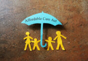 Image showing a paper umbrella cutout with the words "Affordable Care Act" and cutout of family members standing under the umbrella. Health insurers say free preventive care will continue while lawsuit is appealed.