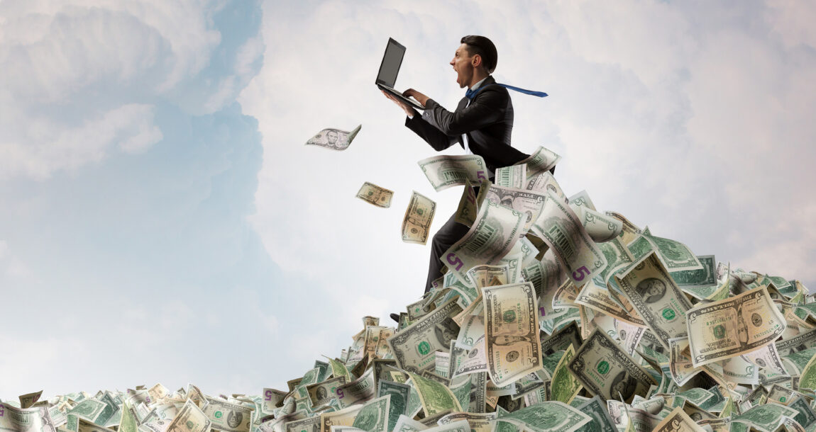 Image of man in a suit holding a laptop atop a large pile of cash.