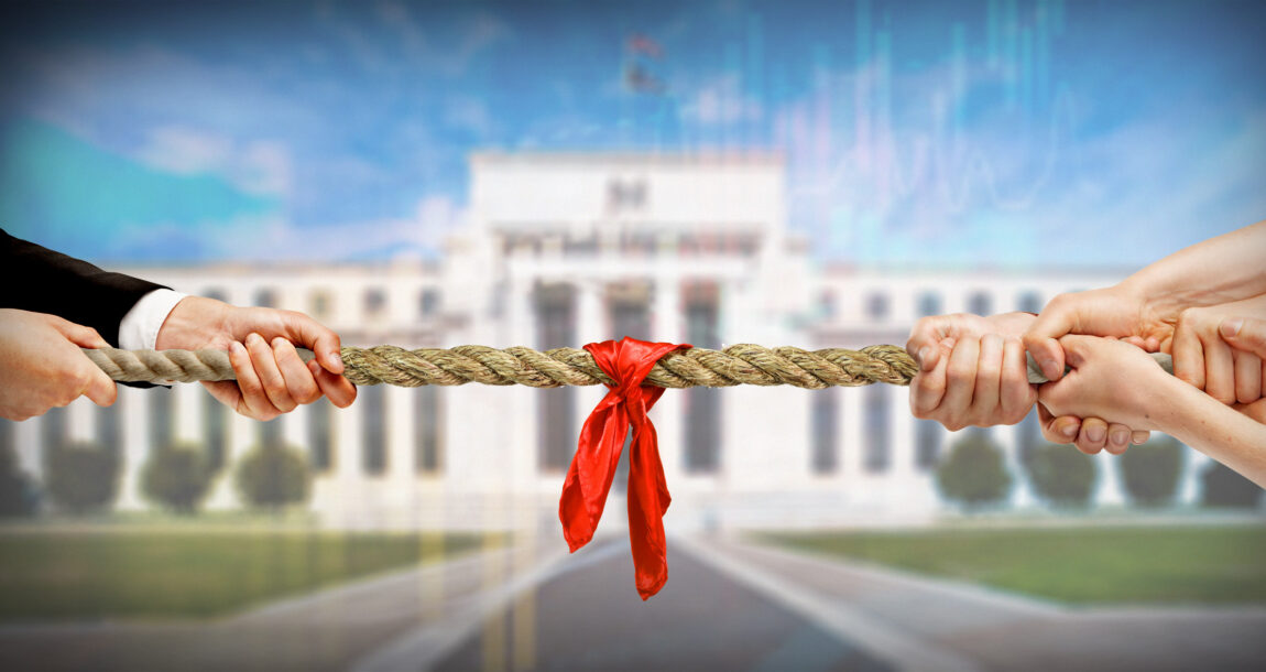 Image of two people having a tug of war in front of the Federal Reserve building. The Fed continues its tug-of-war with inflation, raises rates again.