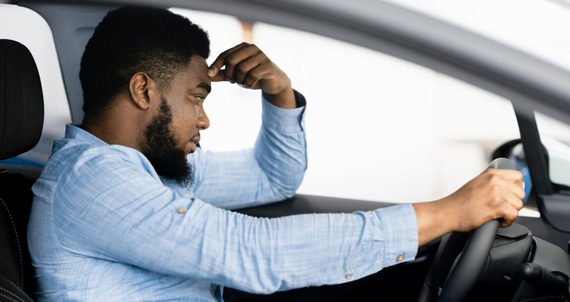 Man sitting in car looking unhappy. Nearly one-third of auto insurance customers see rate increase, study finds.