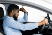 Man sitting in car looking unhappy. Nearly one-third of auto insurance customers see rate increase, study finds.