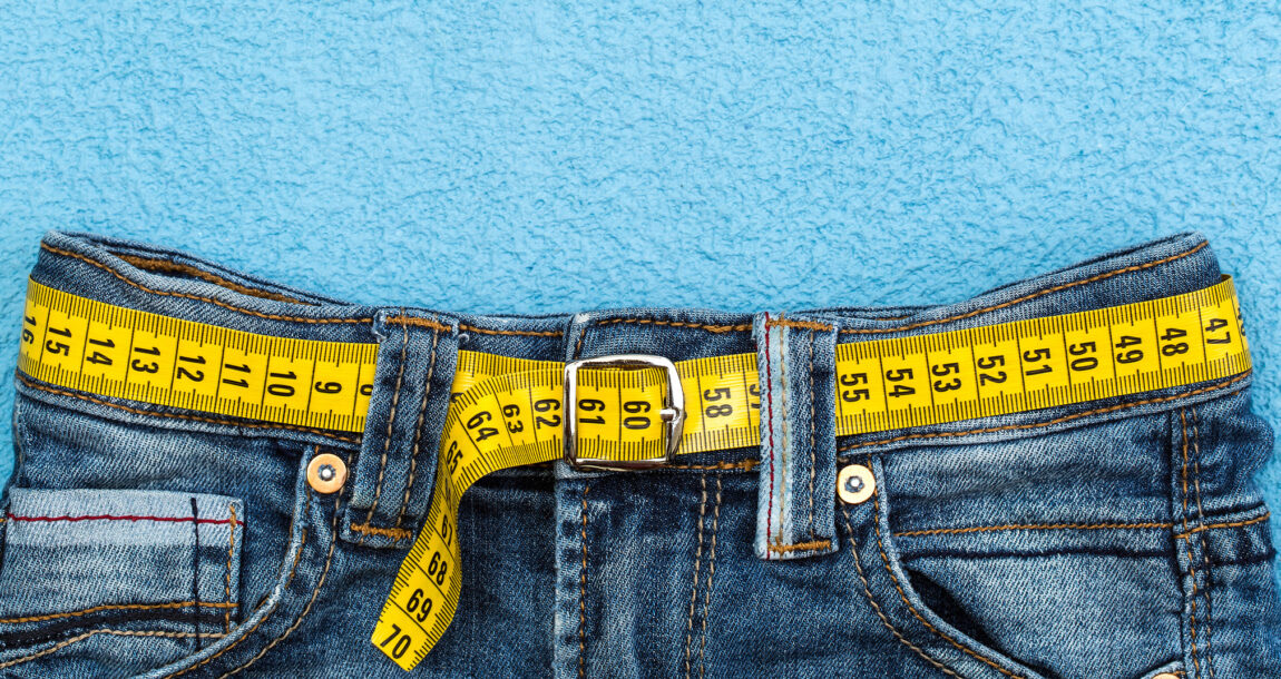 Image of a pair of blue jeans with a measuring tape in place of a belt. Popular weight loss drugs like Ozempic may spur premium increases.