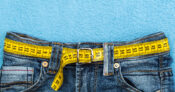Image of a pair of blue jeans with a measuring tape in place of a belt. Popular weight loss drugs like Ozempic may spur premium increases.
