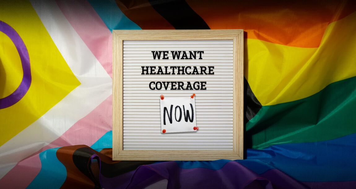 Image shows a sign asking for healthcare coverage against a transgender pride backdrop.