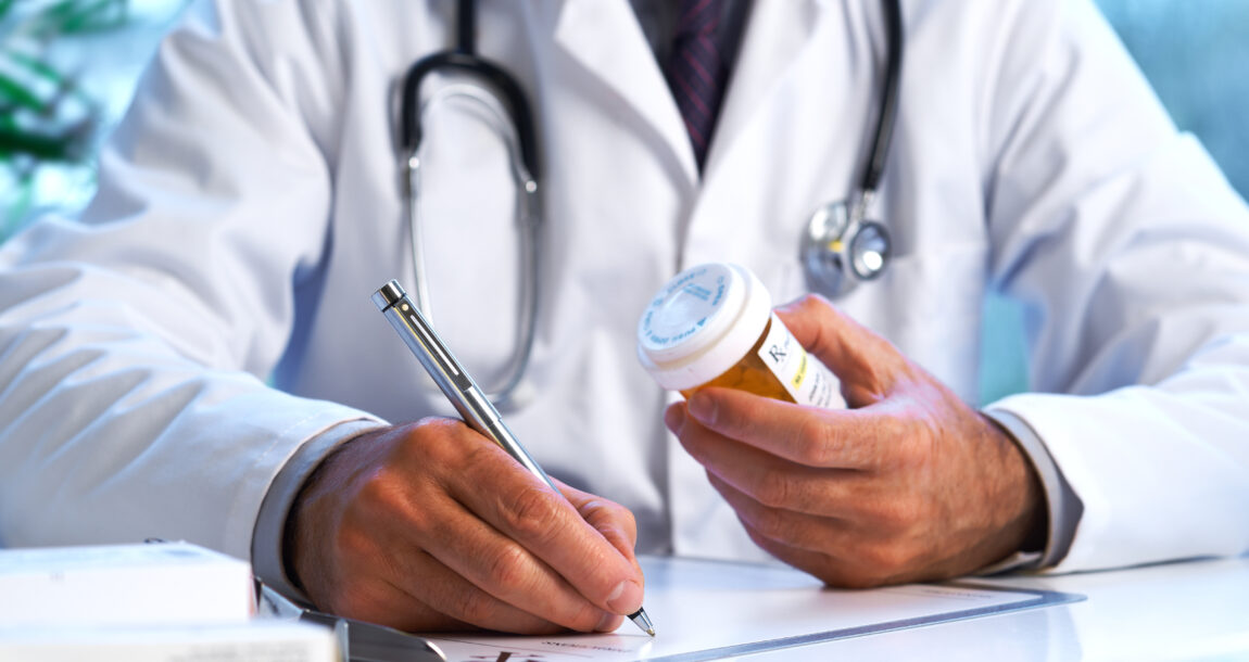 Image of person in a medical smock holding a prescription bottle and writing something on a pad of paper.