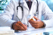 Image of person in a medical smock holding a prescription bottle and writing something on a pad of paper.