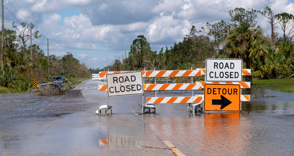 Hurricane flooded street with road closed signs blocking driving of cars. Safety of transportation during natural disaster concept.