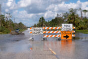 Hurricane flooded street with road closed signs blocking driving of cars. Safety of transportation during natural disaster concept.