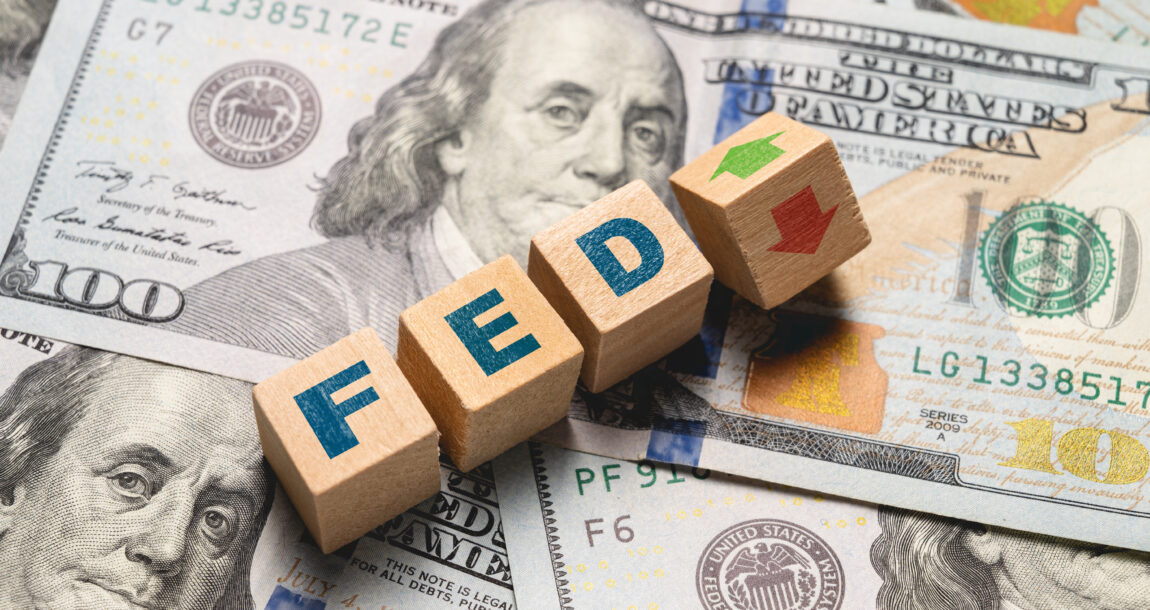 Image of $100 bills with blocks spelling out "FED" and up and down arrows superimposed.