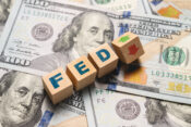 Image of $100 bills with blocks spelling out "FED" and up and down arrows superimposed.