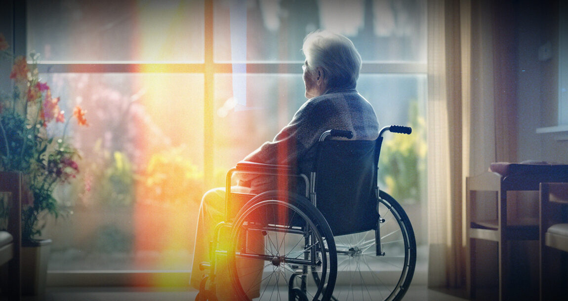 Elderly person sitting in a wheelchair, staring out a window.