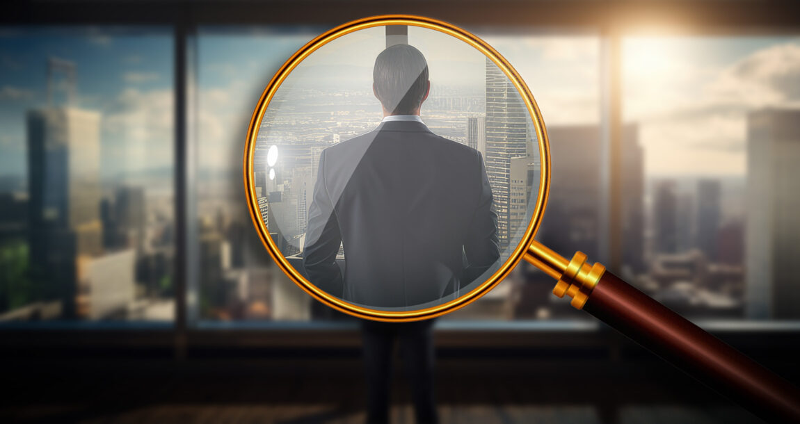 Magnifying glass showing a close up view of person in a business suit looking out over a financial district. Need-for-financial-advice-drives-more-secondary-accounts-to-wealth-management-firms.