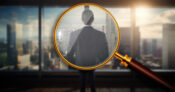 Magnifying glass showing a close up view of person in a business suit looking out over a financial district. Need-for-financial-advice-drives-more-secondary-accounts-to-wealth-management-firms.