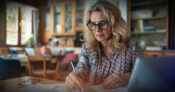 Image of woman sitting at a desk, with pen in hand, working on finances. Study-finds-women-taking-on-more-financial-responsibility.