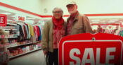 Image of an older couple dressed in inexpensive clothing and shopping in the bargain sales section of a clothing store. The-Decumulation-Paradox--Understanding-why-retirees-underspend.