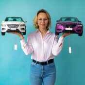 Photo of woman holding a model car in each hand with a pricetag hanging off of each. Skyrocketing auto insurance costs send consumers shopping.