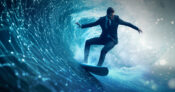 Photo illustration of a man in business suite riding a wave on a surfboard. 5-ways-startups-can-survive-insurtechs-second-wave.