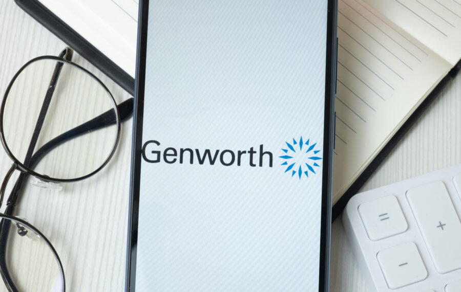 Smartphone with Genworth logo on screen sitting on a desk with financial reports and a pair of eyeglasses. Genworth reports strong third quarter earnings.