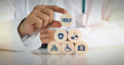 Photo illustration of a person stacking building blocks that have various insurance symbols on them. The-insurance-industry-2025--Whats-ahead.