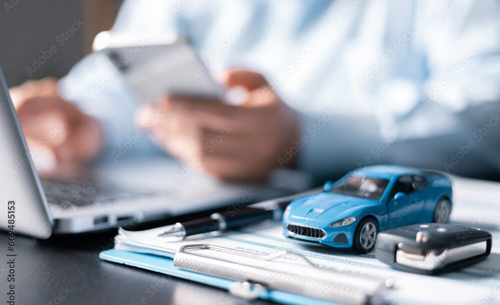 Photo illustration of insurer filling out a form with a small model auto on the form. N.Y. fines auto insurers $20M for timely reporting failure.