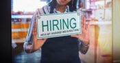 Photo illustration of a person holding a sign that says "Hiring. We've got insurance and everything." Study-Small-businesses-see-benefits-as-key-to-attract-retain-quality-talent.