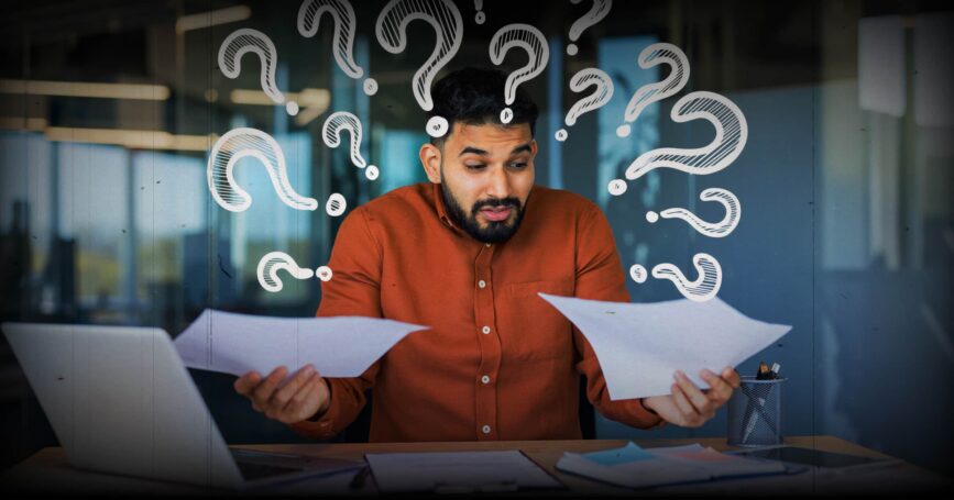 Image shows a man with pieces of paper in both hands and question marks above his head.