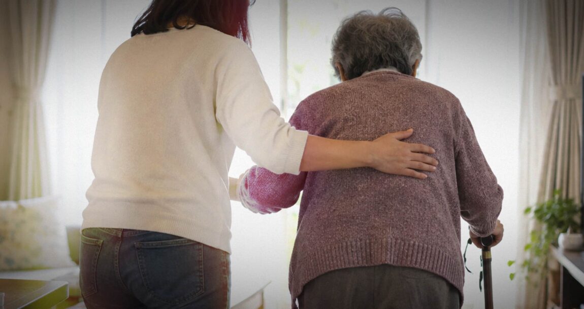 Image shows a woman with her hand on the back of another, older woman.